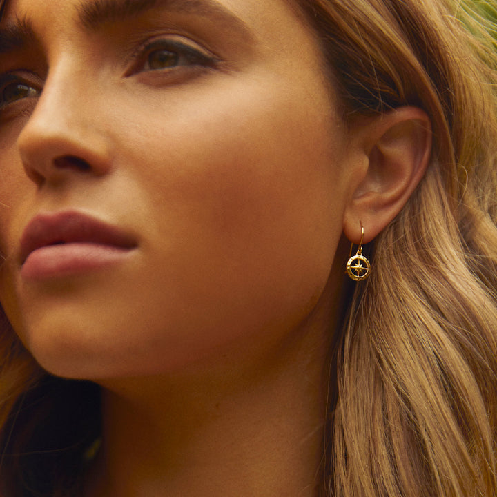 Close-up of a woman wearing a gold compass-earrings