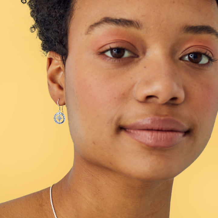 Close-up of a person wearing silver compass earrings with a yellow background