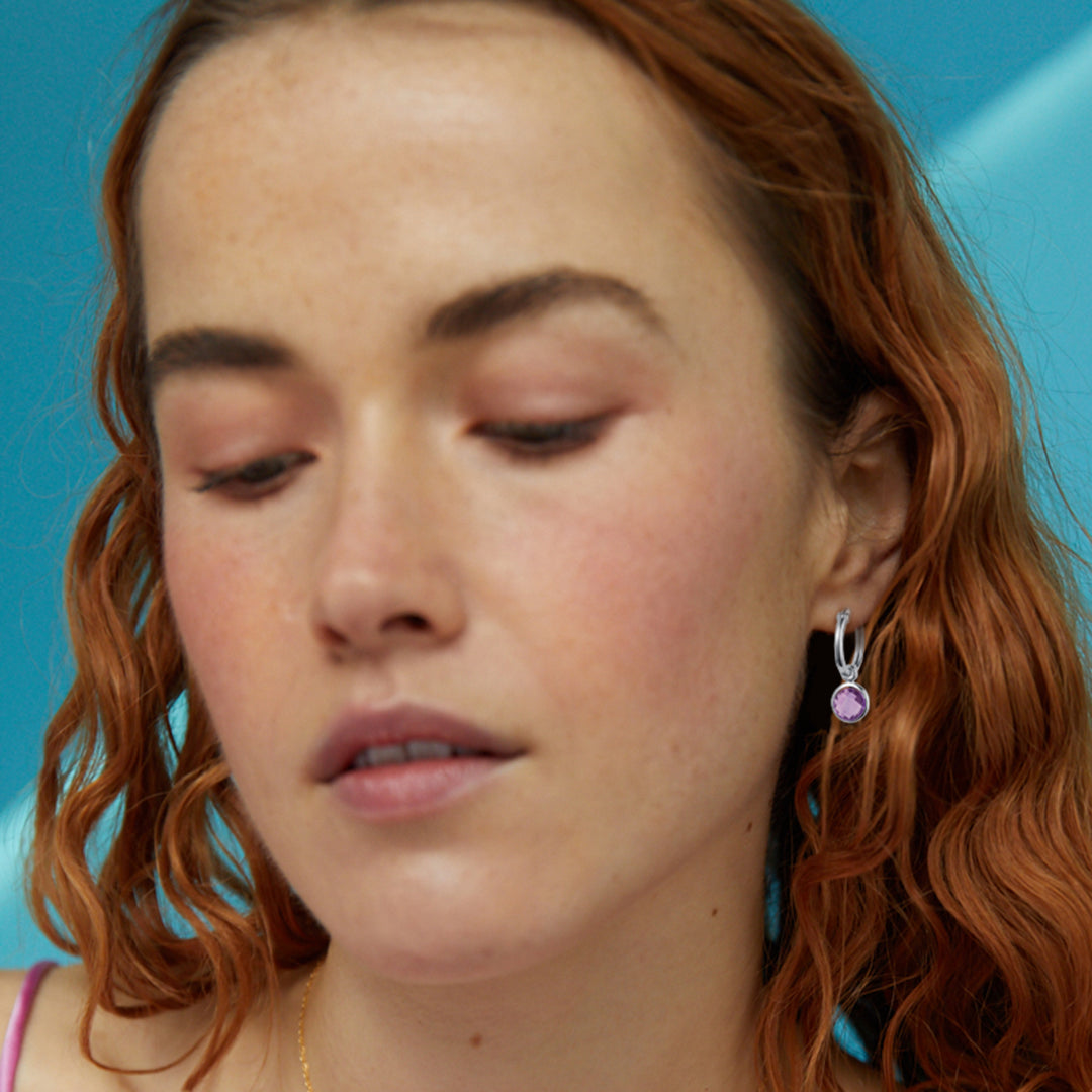 Close-up of a model with red hair wearing sterling silver amethyst huggie hoop earrings
