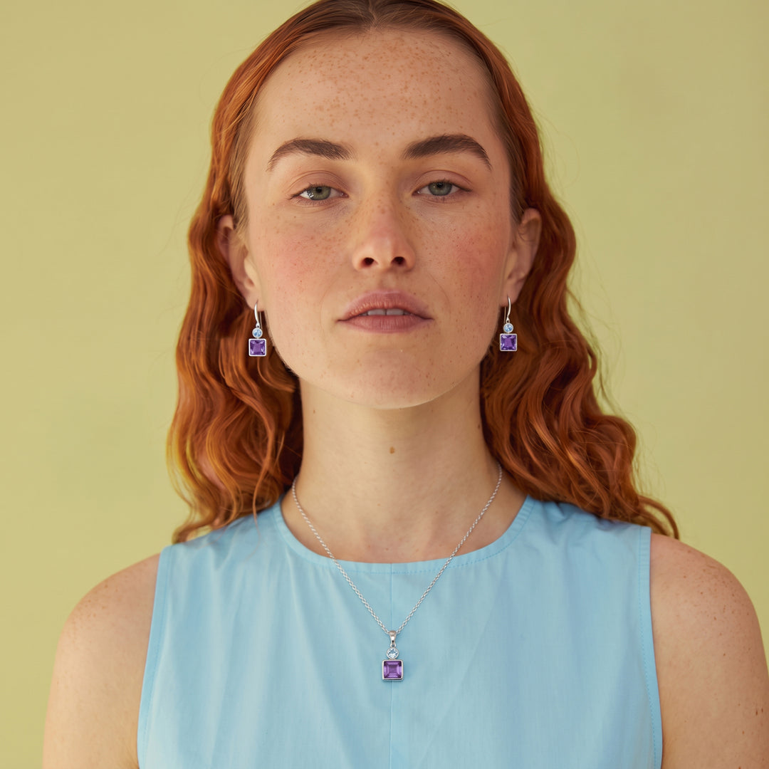 Woman wearing square amethyst and oval blue topaz drop earring and matching necklace in sterling silver