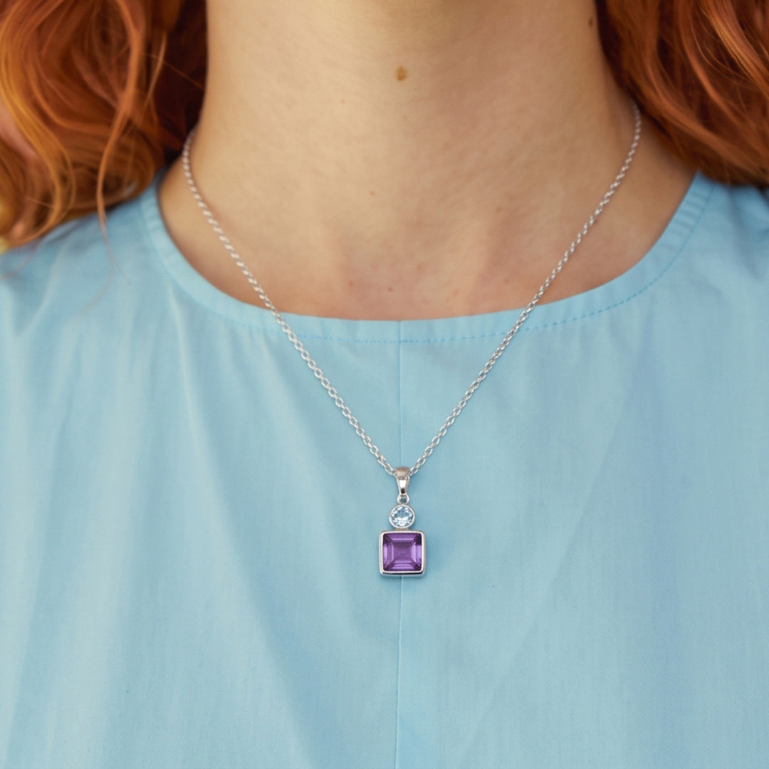 Close-up of woman wearing a square amethyst and oval blue topaz pendant necklace in sterling silver