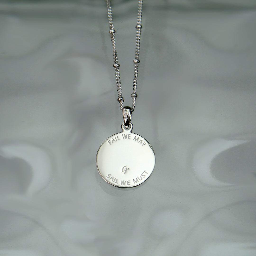 Reverse side of a silver anchor charm necklace with engraved message.
