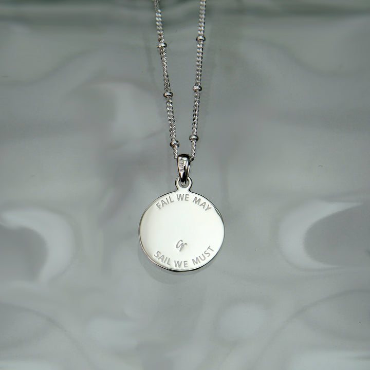 Reverse side of a silver anchor charm necklace with engraved message.