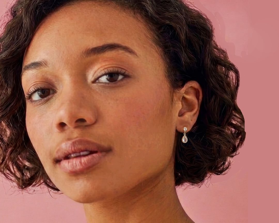 Woman wearing two stone white topaz stud  drop earrings in gold vermeil.