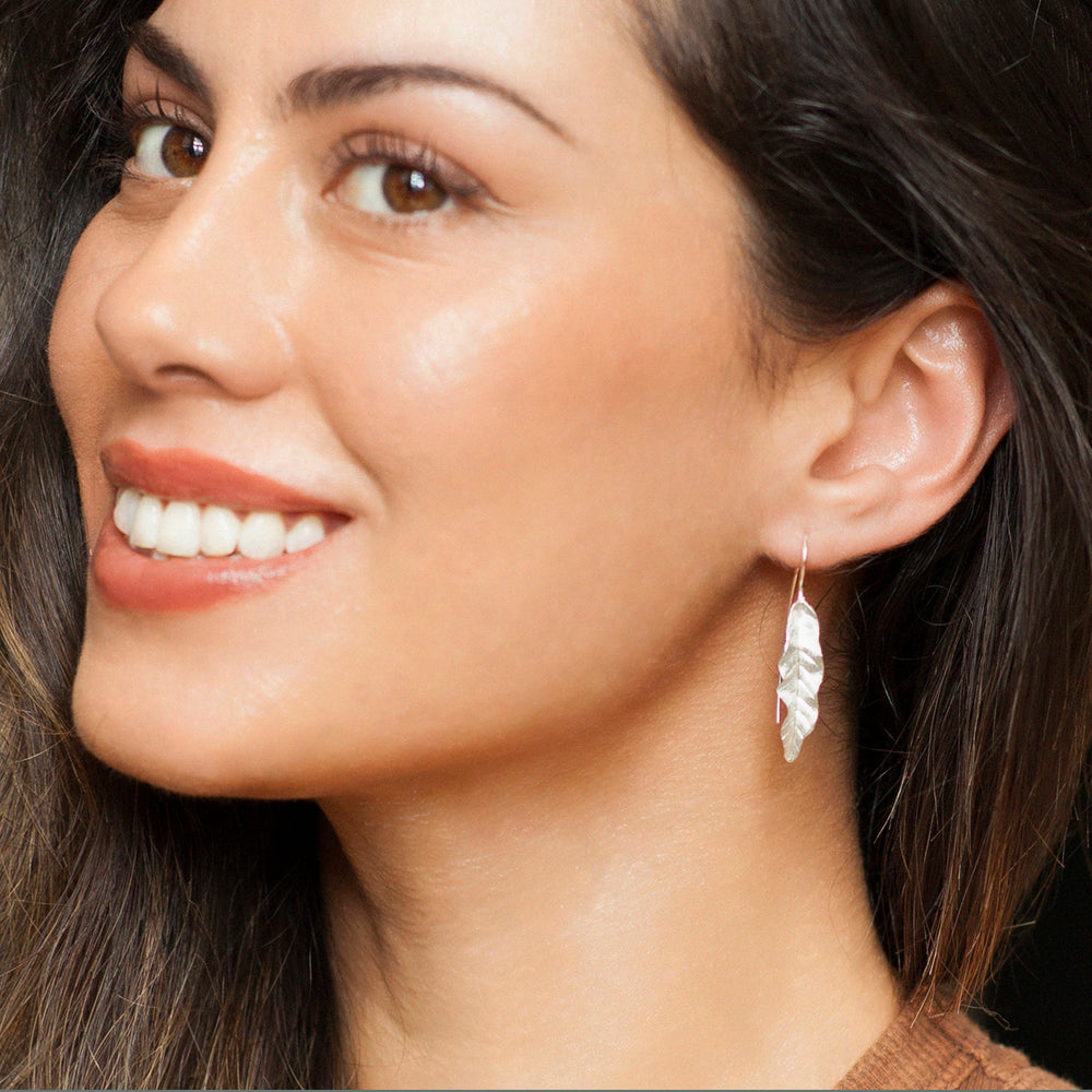 Close-up of a woman wearing silver tropical leaf earrings 