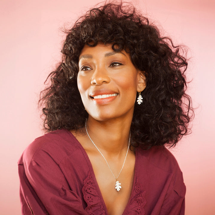 Woman wearing a silver and gold leaf necklace and matching earrings with a burgundy top
