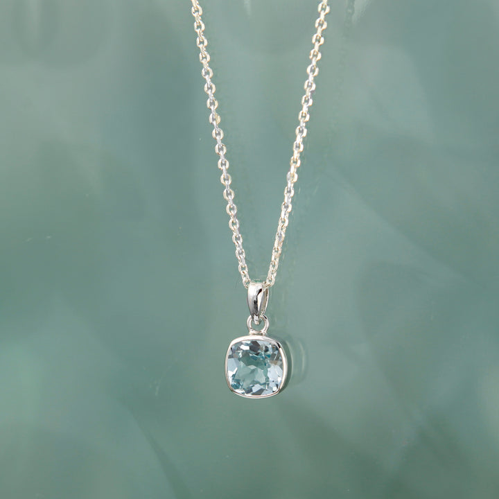 Silver necklace with a blue topaz pendant on a light green background