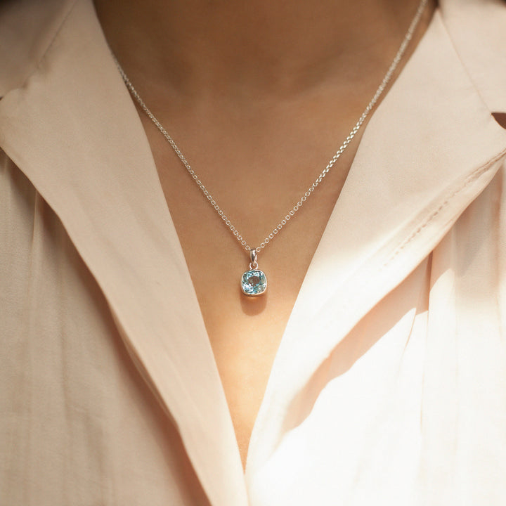 Necklace with a blue gemstone pendant worn by a person in a light-colored shirt.