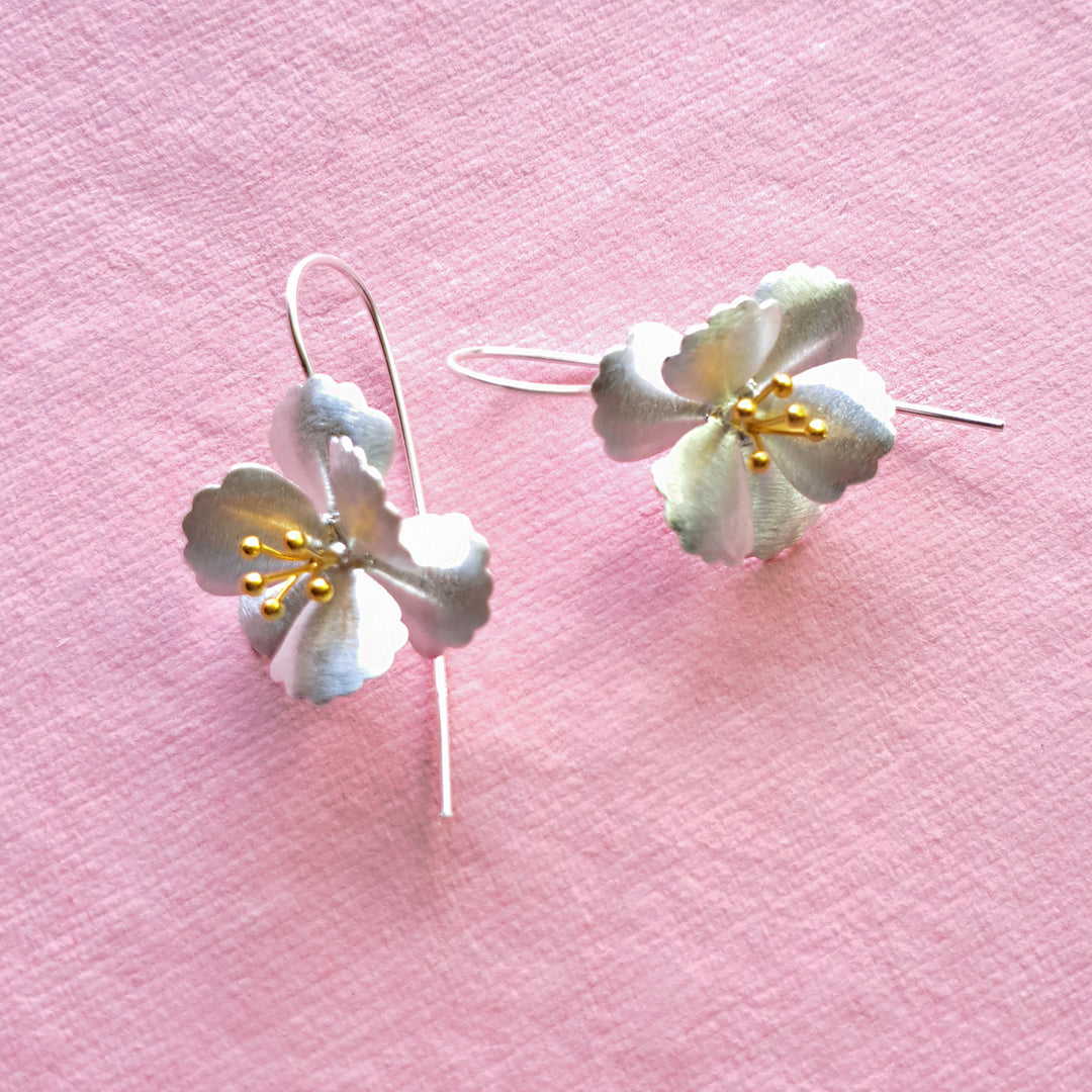 Large silver and gold cherry blossom drop earrings on a pink background showing gold stamen detail