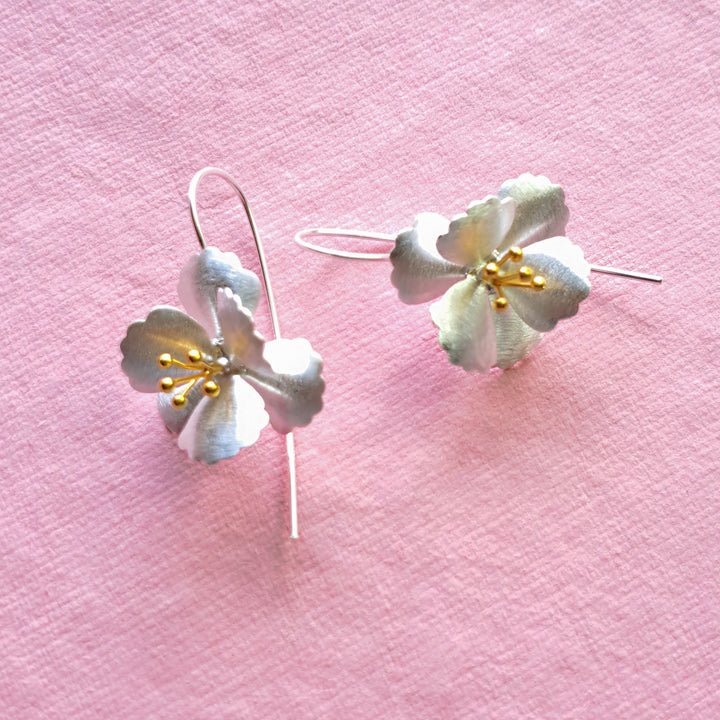 Large silver and gold cherry blossom drop earrings on a pink background showing gold stamen detail