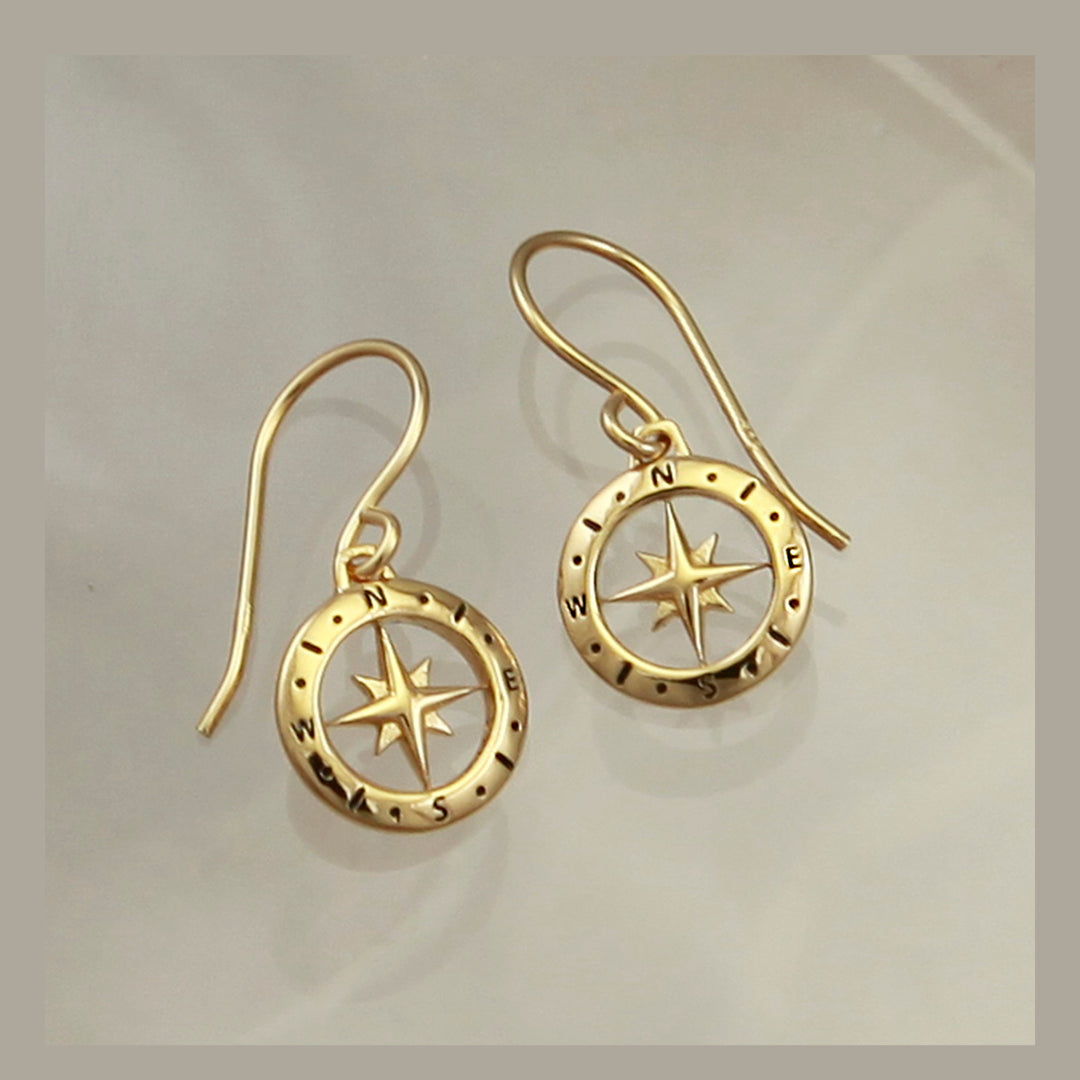 Gold compass earrings with star design on a light gray background