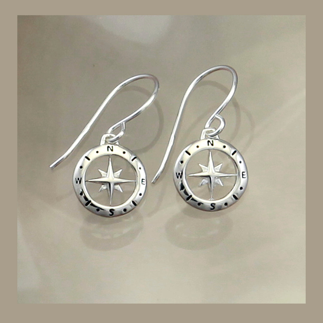 Silver compass earrings on a beige background