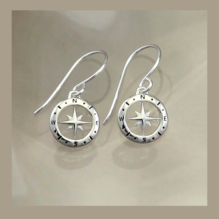 Silver compass earrings on a beige background