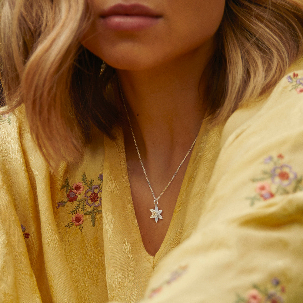 Close-up of a person wearing a silver and gold daffodil necklace and a yellow blouse