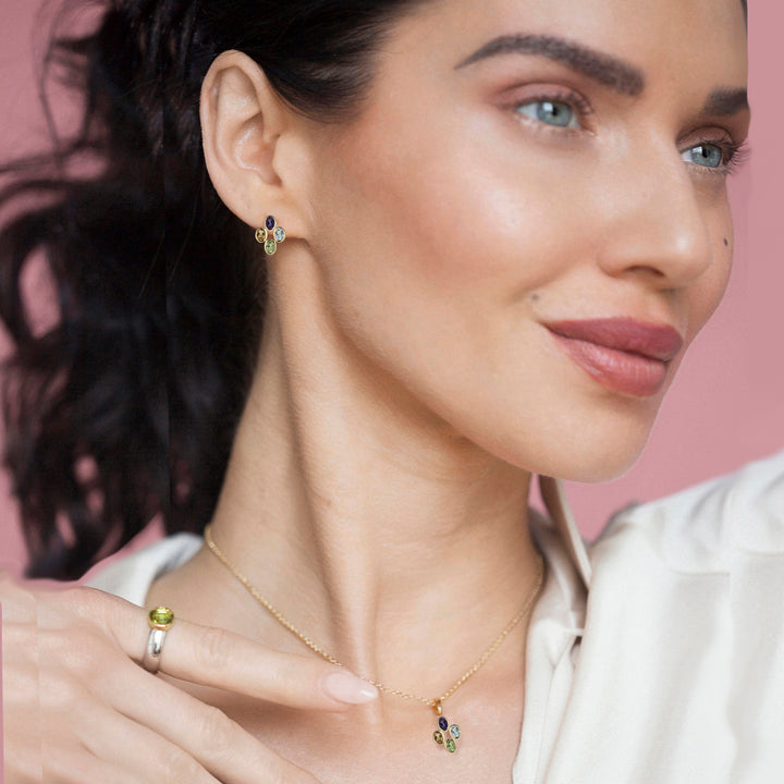 Woman wearing gold earrings and necklace with four gemstones against a pink background