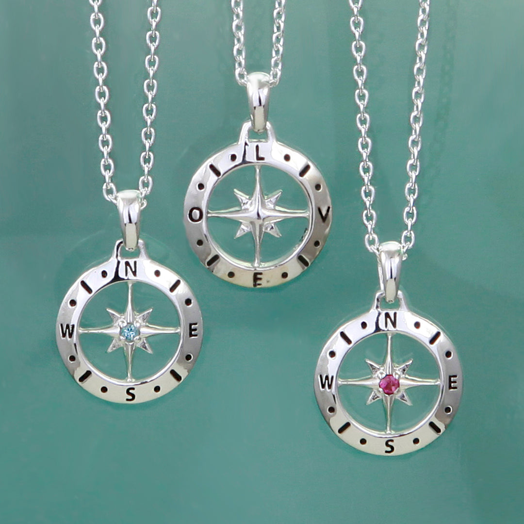 Three silver compass necklaces with gemstones showing front with birthstones and the back spelling LOVE on a green background