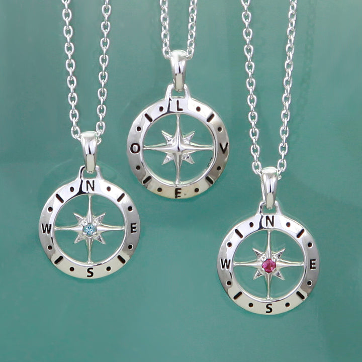 Three silver compass necklaces with gemstones showing front with birthstones and the back spelling LOVE on a green background