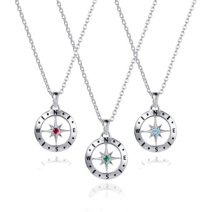 Three silver compass necklaces with ruby, emerald and blue topaz gemstones on a white background