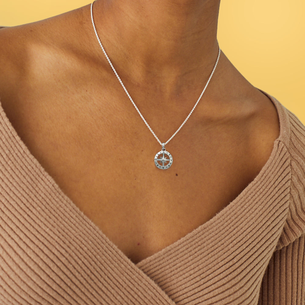 Model wearing a dainty silver compass necklace which spells out LOVE 