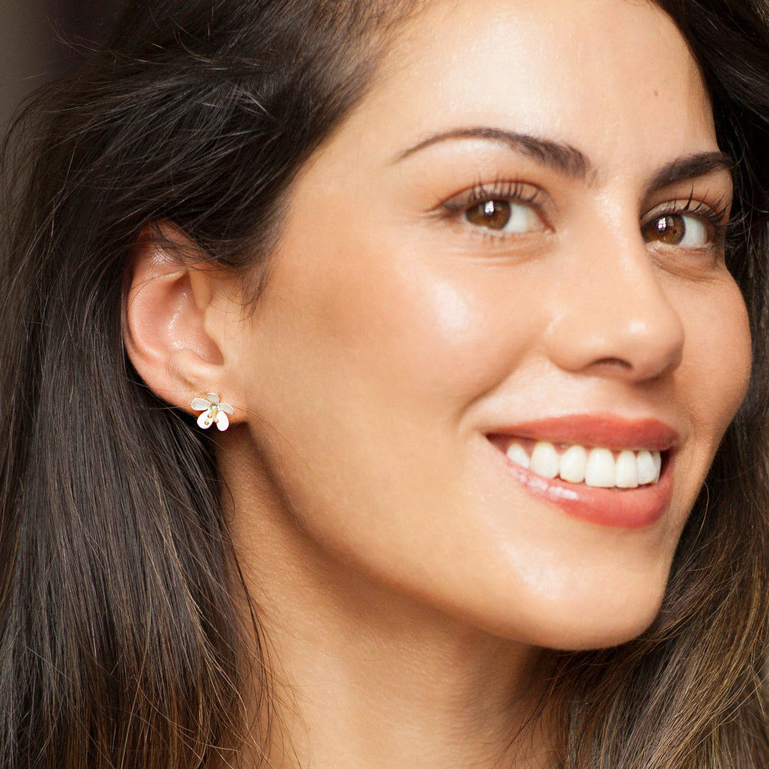 Close-up of a woman wearing silver and gold flower stud earring
