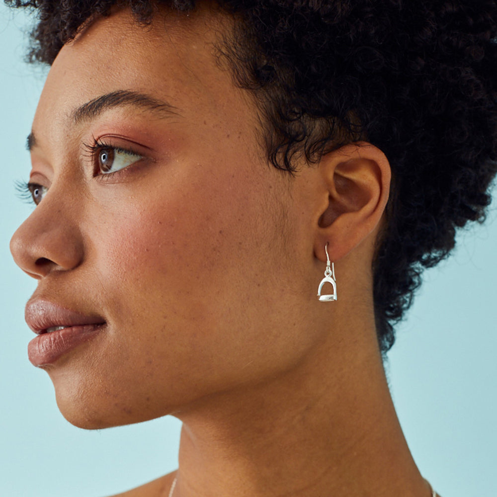 Close-up of a woman wearing a silver stirrup earring against a light blue background
