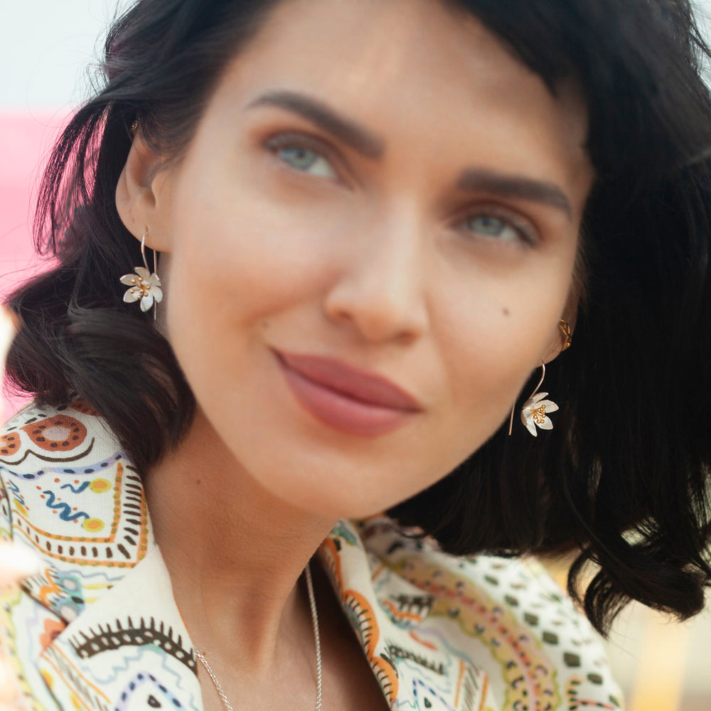 Close-up of a woman wearing floral silver earrings gold centers 
