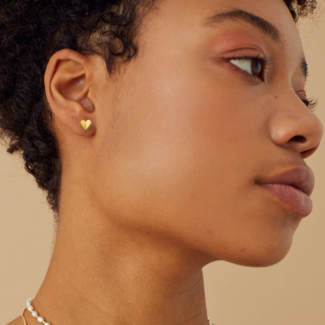Close-up of a person wearing gold heart-shaped earrings against a beige background