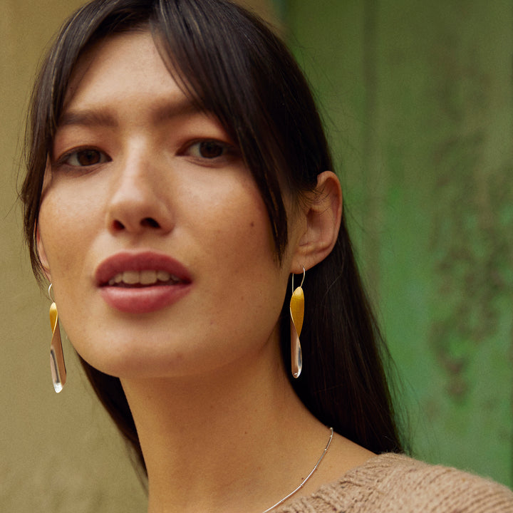 Woman wearing silver and gold earrings with a green background