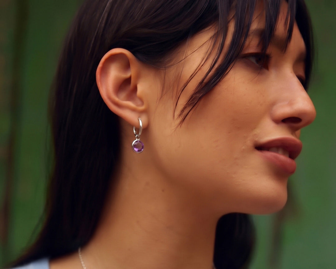 Side view of woman wearing a sterling silver huggie hoop earring with an amethyst drop.