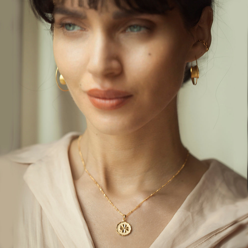 woman wearing a gold four leaf clover necklace and a beige blouse
