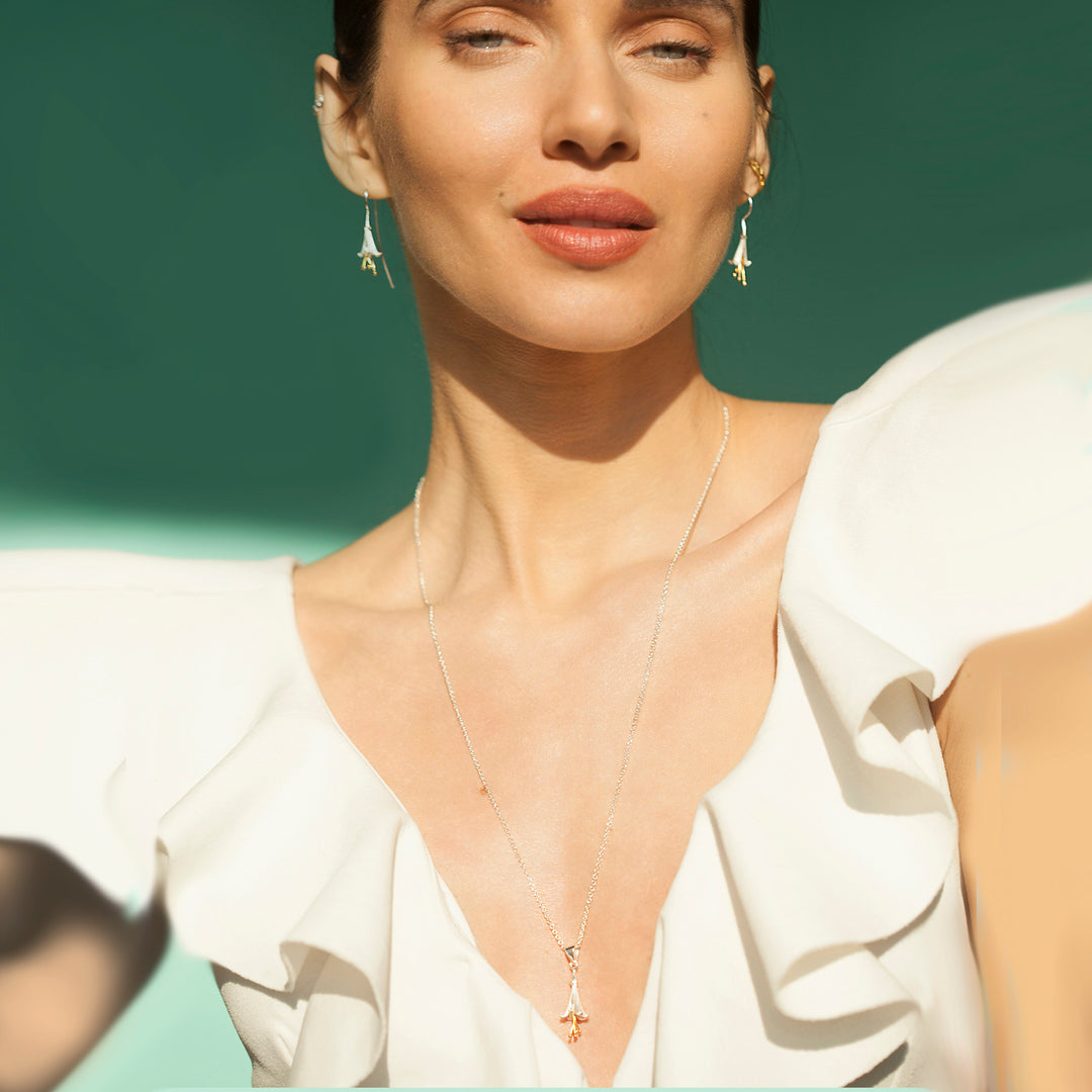 Woman wearing a silver flower necklace and matching earrings against a green background