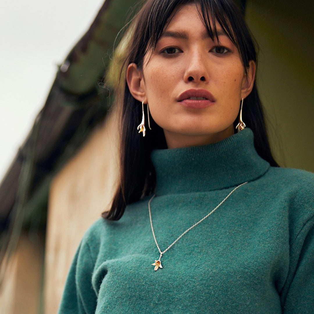 Woman wearing a silver and gold flower jewellery set on green sweater
