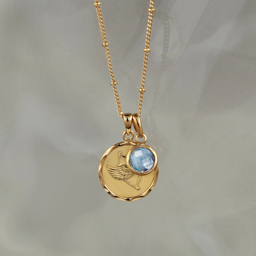 Gold zodiac pendant  with a Sagittarius star sign and a blue topaz December birthstone charm on gray background