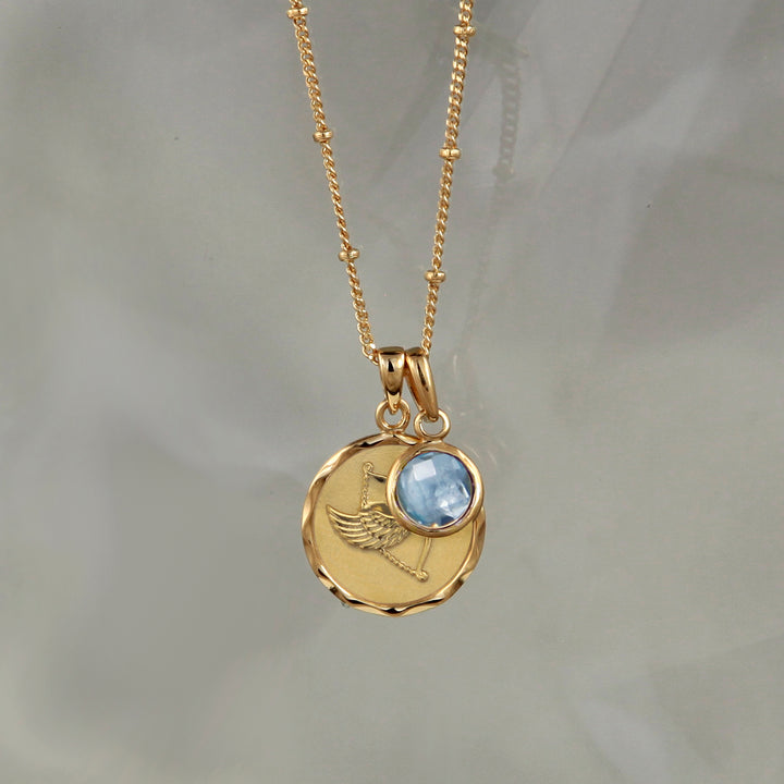 Gold zodiac pendant  with a Sagittarius star sign and a blue topaz December birthstone charm on gray background