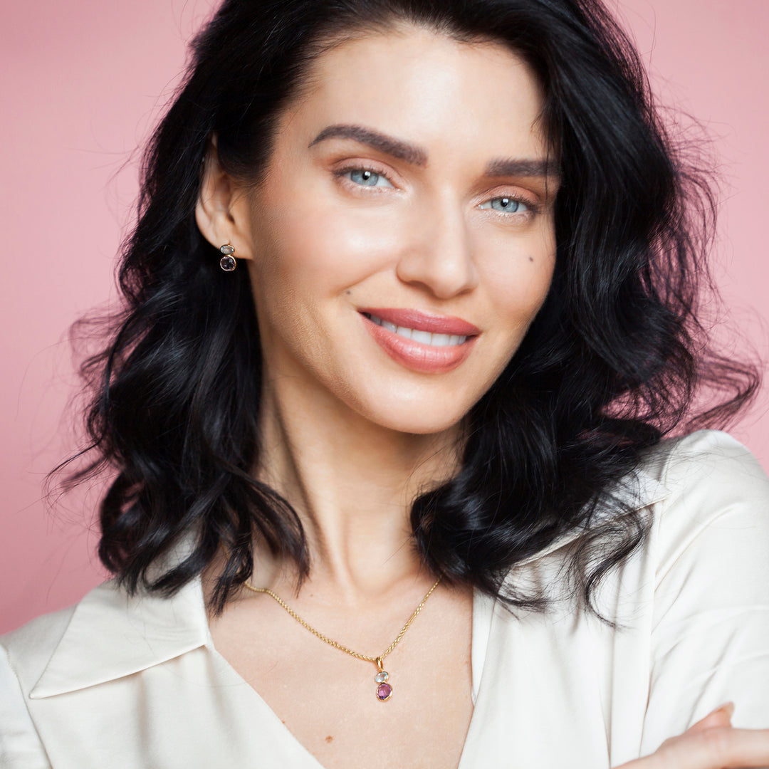Woman wearing matching gold necklace and stud earrings set with amethyst and blue topaz gemstones