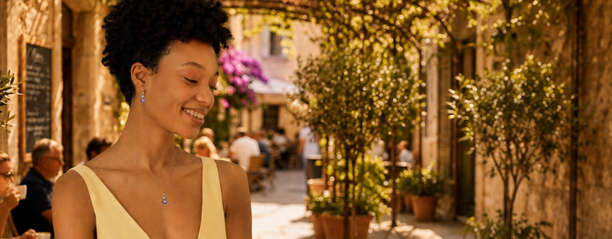 Smiling woman wearing amethyst and blue topaz earring and necklace set in gold vermeil in a cafe setting.