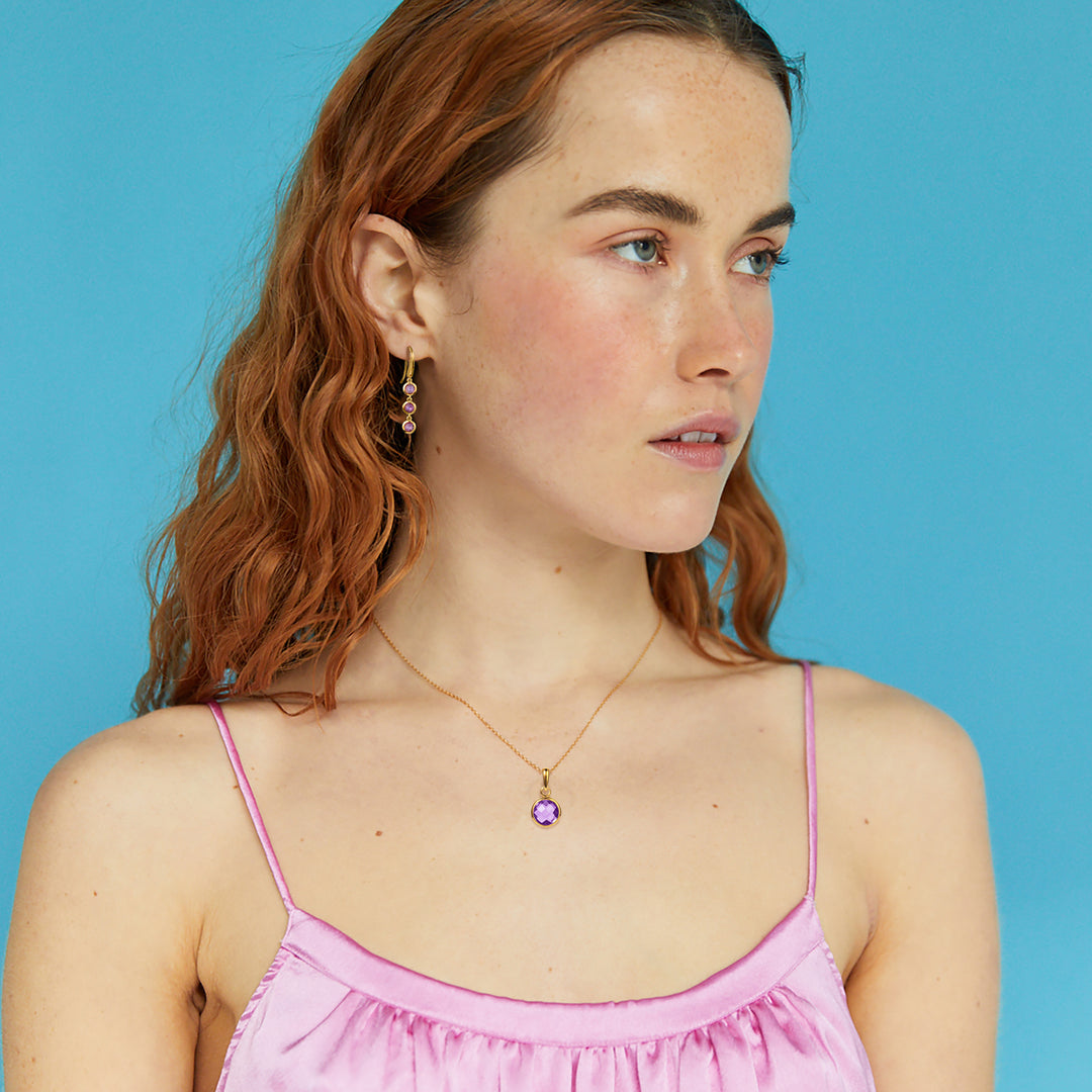 Model wearing a gold and amethyst earring and necklace set against a blue background