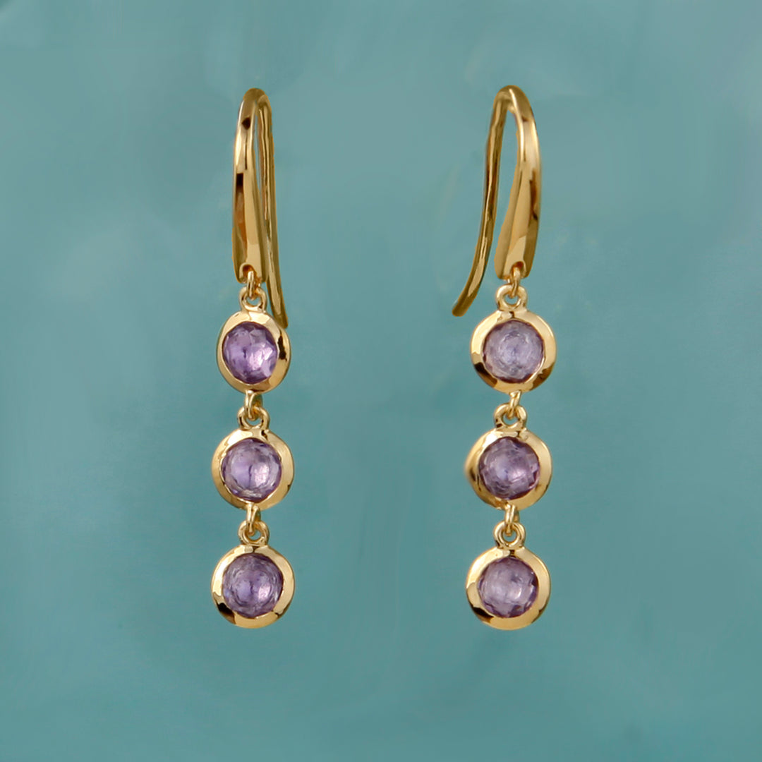 Gold earrings with purple gemstones on a teal background