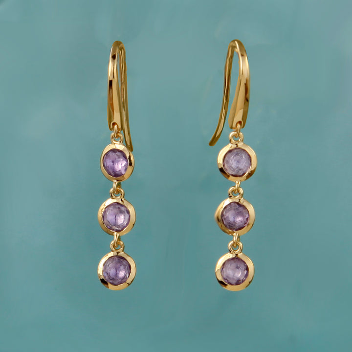 Gold earrings with purple gemstones on a teal background