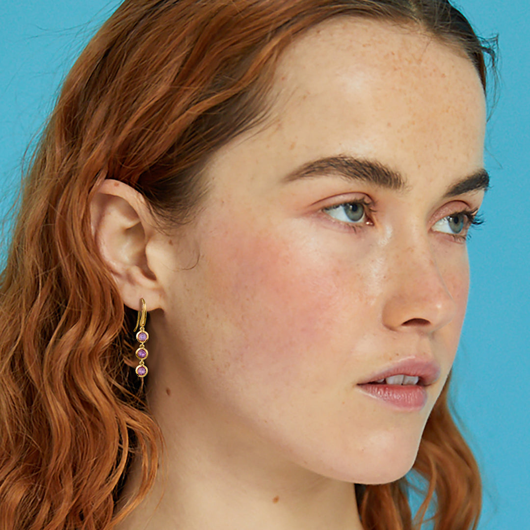 Model wearing a gold three stone drop earring in gold vermeil with natural amethyst