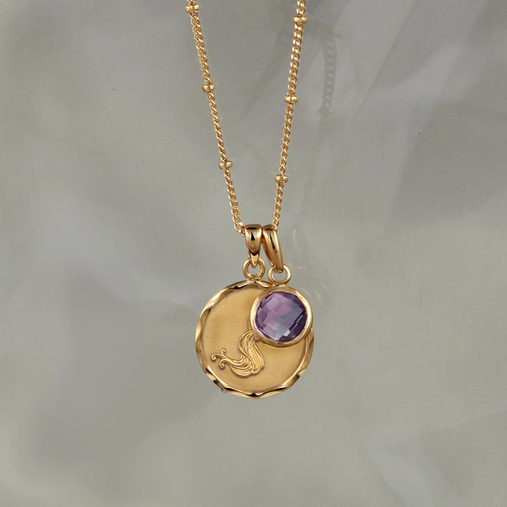 Gold Aquarius necklace with an amethyst February birthstone on gray background
