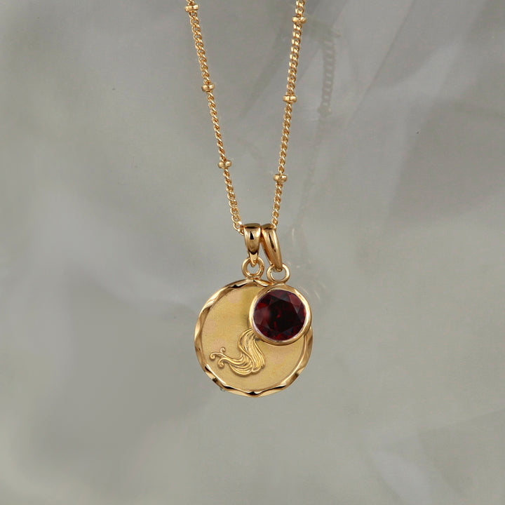 Gold Aquarius necklace with garnet January birthstone on gray background