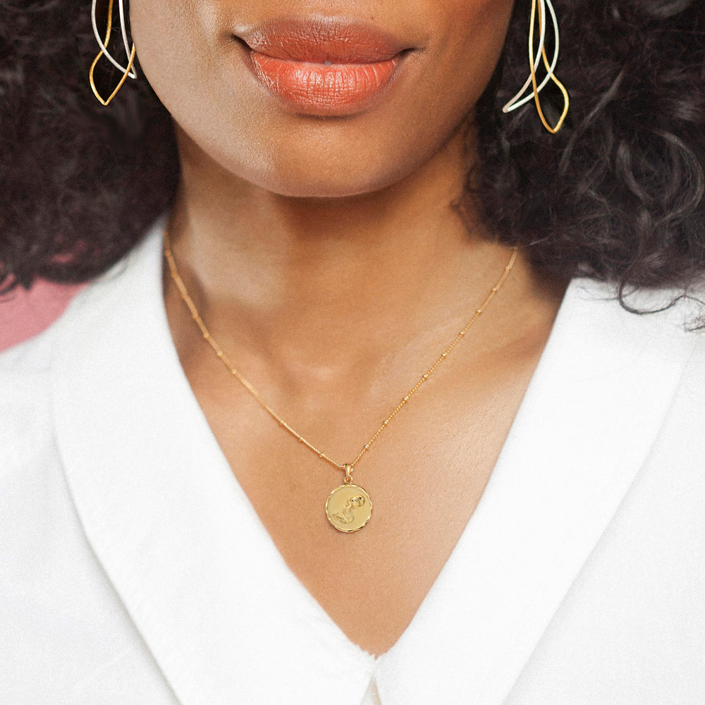 Woman wearing a gold zodiac necklace with an aquarius design and white blouse