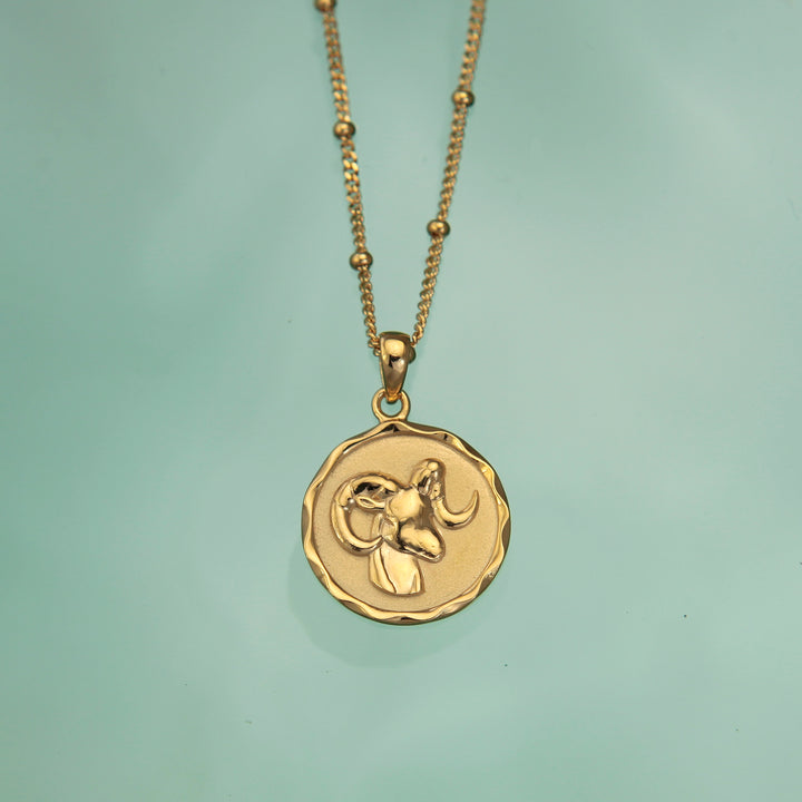 Gold vermeil Aries zodiac star sign pendant necklace against a coloured background