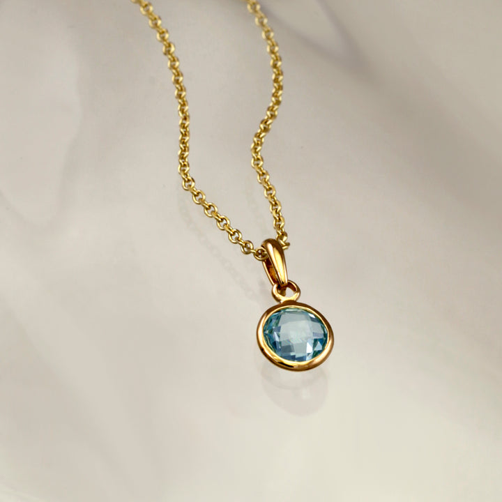 Blue topaz gemstone pendant set in gold vermeil on a gray background