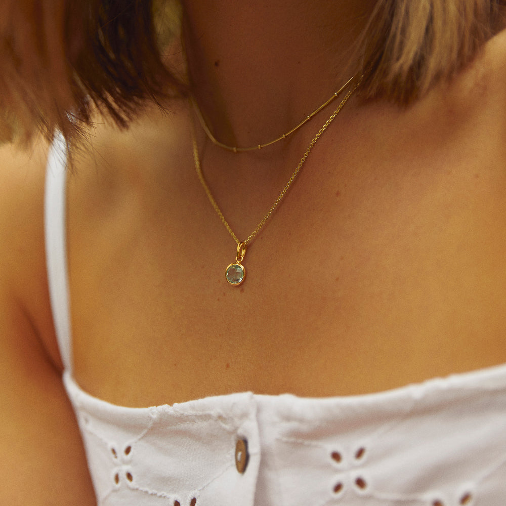 Close-up of model wearing a gold necklace with a blue gemstone pendant