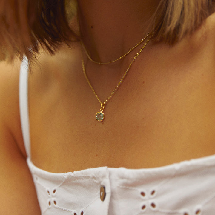 Close-up of model wearing a gold necklace with a blue gemstone pendant