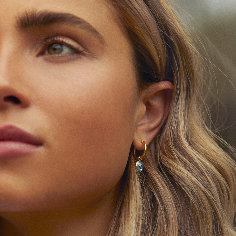 Model wearing gold hoop earrings with blue gemstone pendants