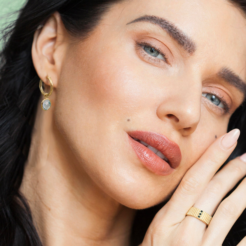 Close-up of a woman wearing gold hoop earrings with blue topaz gemstones.