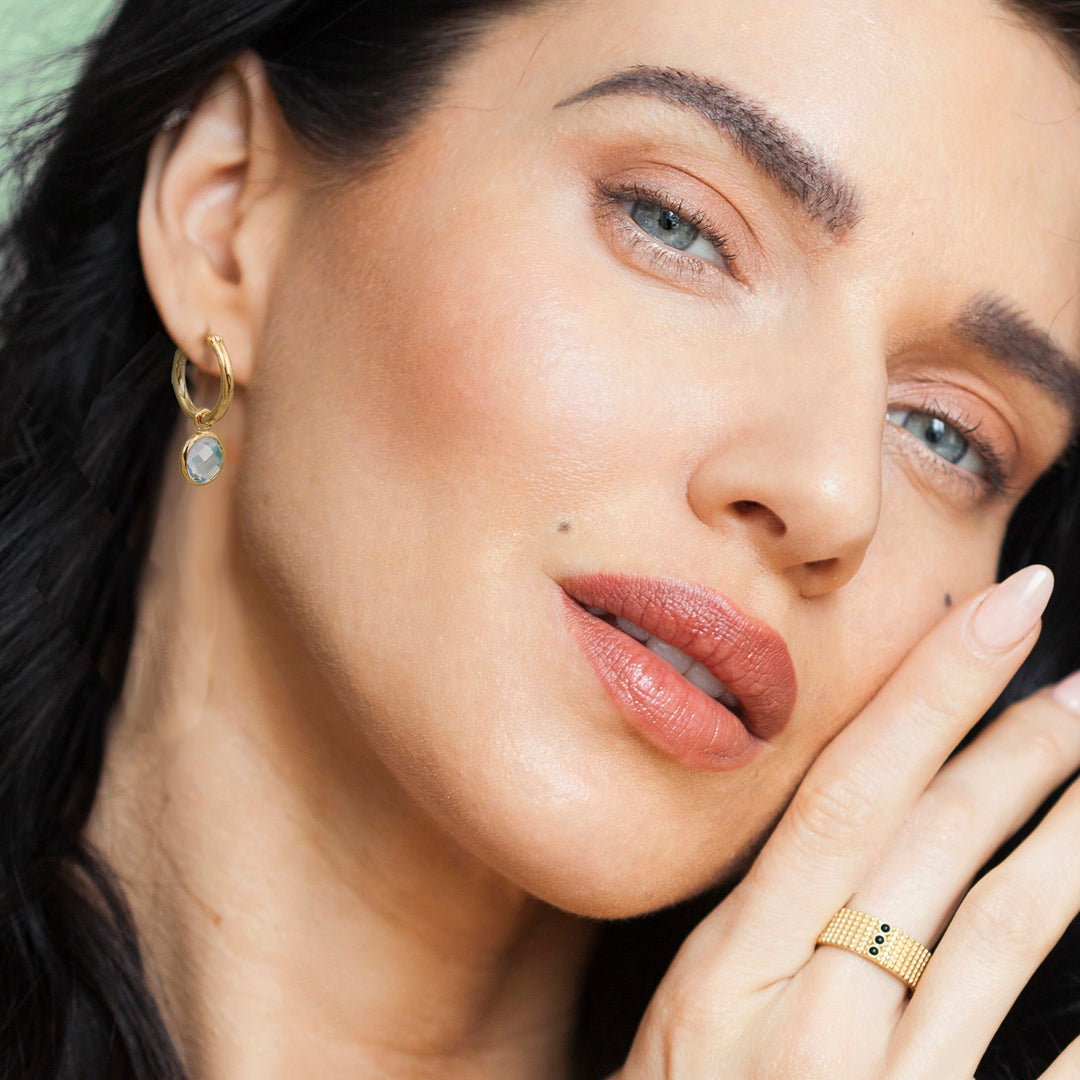 Close-up of a woman wearing gold hoop earrings with blue topaz gemstones.